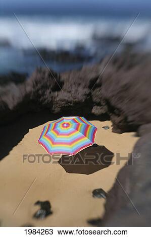Brightly Colored Beach Umbrella In A Sandy Circle Surrounded By Lava Rock Next To The Ocean. View Large Photo Image Stock Image - Brightly Colored Beach Umbrella In A Sandy Circle Surrounded By Lava Rock Next To The Ocean.. Fotosearch