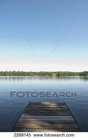 Stock Photography - End of a wooden dock on a tranquil lake with blue sky; kenora ontario canada. Fotosearch