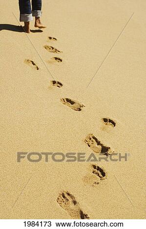 Stock Image - Footprints In Sand With Legs (Wearing Jeans) And Feet At Top Of Picture.. Fotosearch