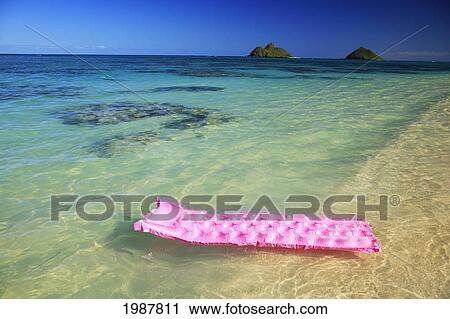 Stock Image - Hawaii, Oahu, Lanikai, Pink Inflated Raft On Clear Ocean Water, Mokulua's In Background.. Fotosearch