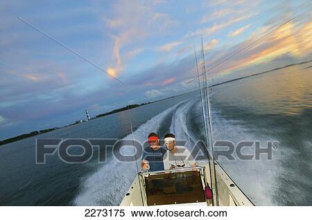 Stock Photography - Men riding in a boat at sunset; north carolina united states of america. Fotosearch