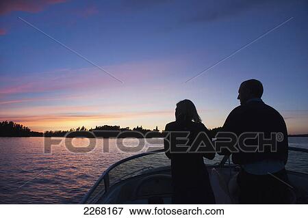 Stock Photo - Middle aged couple travelling by motorboat in the lake of the woods at sunset; kenora ontario canada. Fotosearch