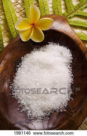 Stock Photograph - Spa Elements, Koa Bowl Filled With Raw Salt, Garnished With Yellow Plumeria And Leaf On Lauhala Mat.. Fotosearch