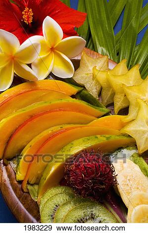 Stock Photo - Studio Shot Pf A Variety Of Tropical Fruit Sliced On A Platter, With Flowers.. Fotosearch