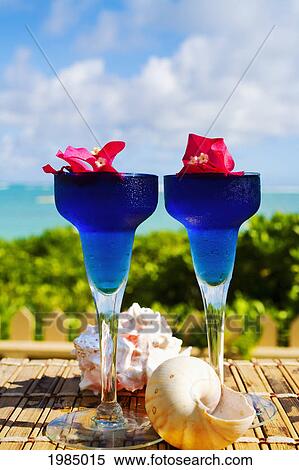 Stock Photography - Two Tropical Cocktails Garnished With Flowers In Outdoor Setting.. Fotosearch