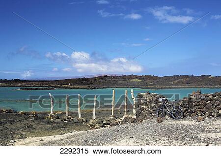 Stock Photography - A bicycle leaning against a stone wall at the shore with a view of the coastline of an hawaiian island; Hawaii united states of america. Fotosearch