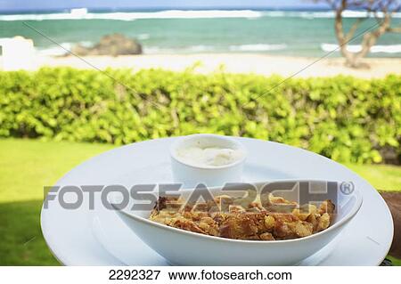Stock Photo - A food item served in a white serving dish with a view of the beach and ocean; Hawaii united states of america. Fotosearch