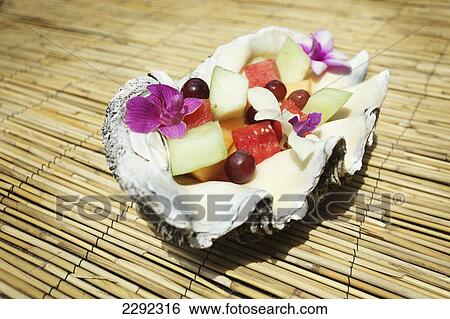 Stock Photograph - A fruit salad with floral garnishes served inside a seashell; Hawaii united states of america. Fotosearch