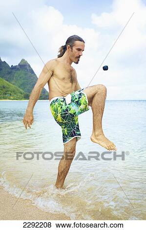Stock Photo - A man bumps a hackey sack with his knee while standing in the shallow water of the ocean; Hawaii united states of america. Fotosearch