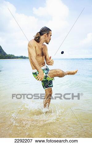 A man kicks a hackey sack while standing in the shallow water of the ocean; Hawaii united states of america View Large Photo Image Stock Photo - A man kicks a hackey sack while standing in the shallow water of the ocean; Hawaii united states of america. Fotosearch