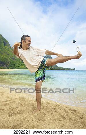 Stock Image - A man plays with his hackey sack in the sand at the water's edge; Hawaii united states of america. Fotosearch