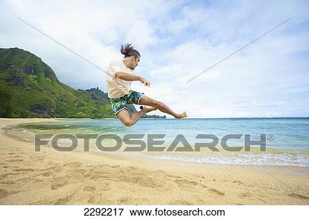 A man takes a leap into the air while playing with a hackey sack on the beach; Hawaii united states of america View Large Photo Image Stock Photo - A man takes a leap into the air while playing with a hackey sack on the beach; Hawaii united states of america. Fotosearch