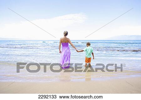 A mother and son hold hands while standing in the shallow water looking out at the ocean; Hawaii united states of america View Large Photo Image Stock Image - A mother and son hold hands while standing in the shallow water looking out at the ocean; Hawaii united states of america. Fotosearch