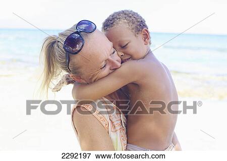 Stock Photo - A mother and son in an embrace on the beach at the water's edge; Hawaii united states of america. Fotosearch