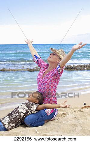 Stock Photograph - A mother and son on the beach at the water's edge with arms outstretched in enjoyment; Hawaii united states of america. Fotosearch