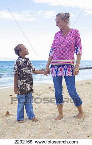 Stock Photo - A mother and son standing in the sand at the water's edge; Hawaii united states of america. Fotosearch