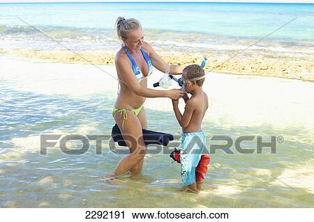 Stock Image - A mother and son with snorkelling gear in the shallow water; Hawaii united states of america. Fotosearch