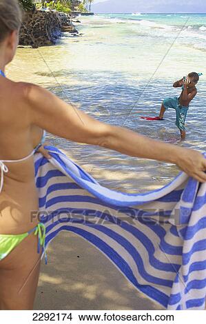 Picture - A mother holds a towel out for her son as he comes out of the water with snorkelling gear; Hawaii united states of america. Fotosearch