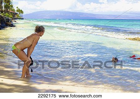 Stock Photography - A mother watches her son snorkelling in the shallow water at the beach; Hawaii united states of america. Fotosearch