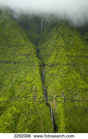 Stock Photograph - A stream flowing down a lush green mountainside with low lying cloud; Hawaii united states of america. Fotosearch