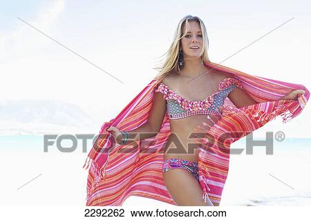 Stock Image - A teenage girl in a bikini holding a wrap with the ocean in the background; Maui hawaii united states of america. Fotosearch
