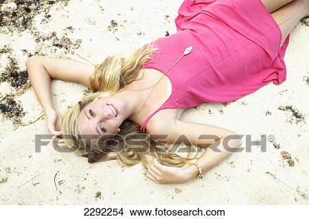 Picture - A teenage girl in a pink dress laying in the sand; Maui hawaii united states of america. Fotosearch