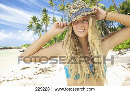 Stock Image - A teenage girl on the beach in a two piece bathing suit and hat; Maui hawaii united states of america. Fotosearch