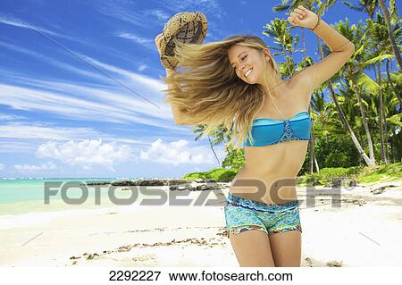 A teenage girl on the beach with her long hair blowing in the wind as she takes off her hat; Maui hawaii united states of america View Large Photo Image Stock Photo - A teenage girl on the beach with her long hair blowing in the wind as she takes off her hat; Maui hawaii united states of america. Fotosearch