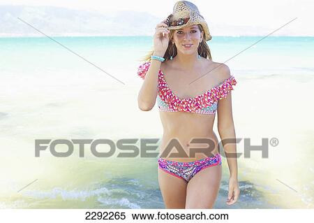 Stock Photography - A teenage girl wearing a bikini and sunhat walking through the shallow ocean water; Maui hawaii united states of america. Fotosearch