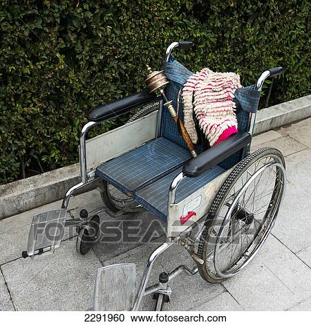 Stock Image - A wheelchair sits on a sidewalk with a blanket and traditional chinese item; Lhasa xizang china. Fotosearch
