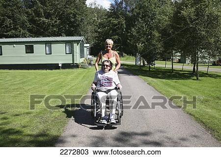 A woman pushes another woman down a path in a wheelchair; Pooley bridge ullswater lake district cumbria england View Large Photo Image Stock Image - A woman pushes another woman down a path in a wheelchair; Pooley bridge ullswater lake district cumbria england. Fotosearch