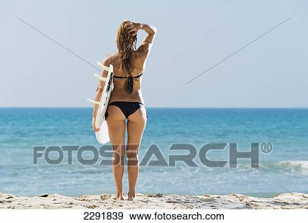 A woman wearing a black bikini stands at the water's edge holding a surfboard; Tarifa cadiz andalusia spain View Large Photo Image Stock Photo - A woman wearing a black bikini stands at the water's edge holding a surfboard; Tarifa cadiz andalusia spain. Fotosearch