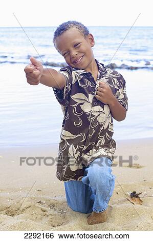 Stock Photograph - A young boy in a silly pose in the sand at the water's edge; Hawaii united states of america. Fotosearch