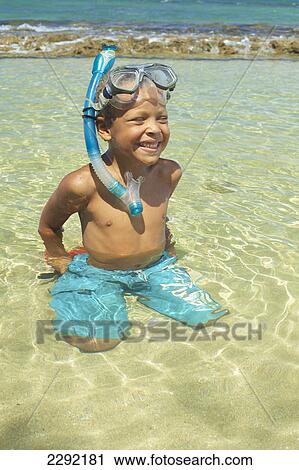 Stock Image - A young boy in the shallow water of the ocean with snorkelling gear; Hawaii united states of america. Fotosearch