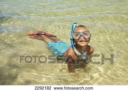 Stock Image - A young boy in the shallow water of the ocean with snorkelling gear; Hawaii united states of america. Fotosearch