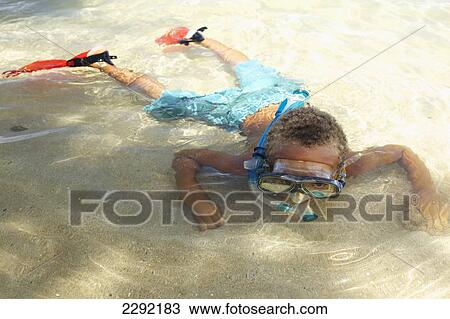 Stock Image - A young boy in the shallow water of the ocean with snorkelling gear; Hawaii united states of america. Fotosearch
