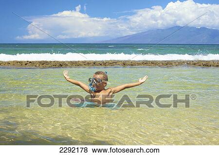 Stock Photo - A young boy in the shallow water of the ocean with snorkelling gear; Hawaii united states of america. Fotosearch