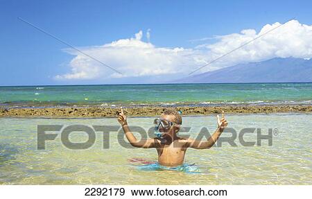 Stock Photo - A young boy in the shallow water of the ocean with snorkelling gear giving the peace sign; Hawaii united states of america. Fotosearch