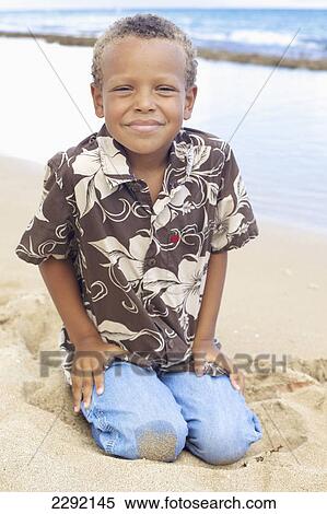 A young boy kneels in the sand at the water's edge; Hawaii united states of america View Large Photo Image Stock Photography - A young boy kneels in the sand at the water's edge; Hawaii united states of america. Fotosearch