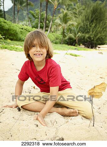 Stock Photo - A young boy plays in the sand on the beach; Hawaii united states of america. Fotosearch