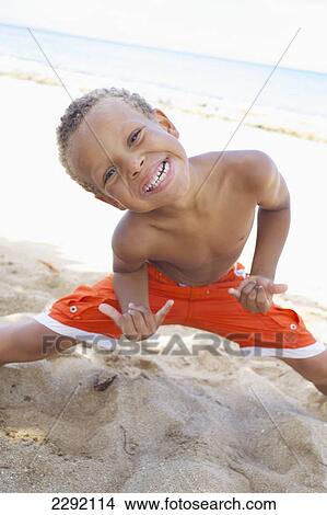 Picture - A young boy poses in a cool stance while standing in the sand by the ocean; Hawaii united states of america. Fotosearch