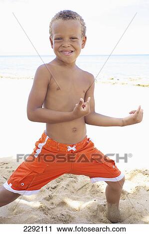 Stock Image - A young boy poses in a cool stance while playing in the sand by the ocean; Hawaii united states of america. Fotosearch