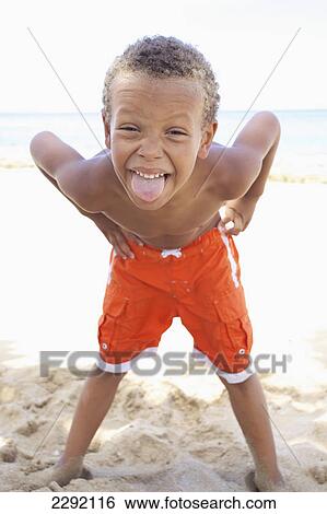 A young boy poses with a silly face while standing in the sand by the ocean; Hawaii united states of america View Large Photo Image Stock Photograph - A young boy poses with a silly face while standing in the sand by the ocean; Hawaii united states of america. Fotosearch