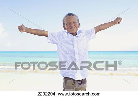 A young boy poses with arms outstretched on the beach at the water's edge; Hawaii united states of america View Large Photo Image Picture - A young boy poses with arms outstretched on the beach at the water's edge; Hawaii united states of america. Fotosearch