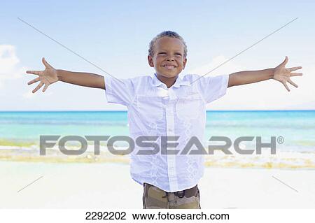 Stock Image - A young boy poses with arms outstretched on the beach at the water's edge; Hawaii united states of america. Fotosearch