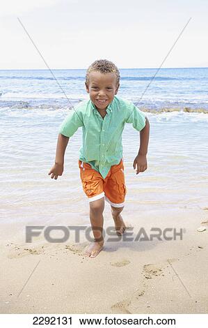 Stock Image - A young boy running in the sand by the ocean; Hawaii united states of america. Fotosearch