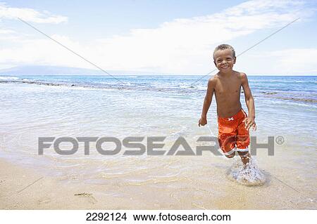 Picture - A young boy runs and plays in the shallow water of the ocean; Hawaii united states of america. Fotosearch