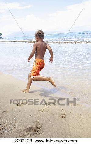A young boy runs and plays in the sand by the ocean; Hawaii united states of america View Large Photo Image Stock Photo - A young boy runs and plays in the sand by the ocean; Hawaii united states of america. Fotosearch