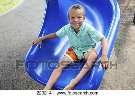 Stock Image - A young boy sits posing at the bottom of a slide; Hawaii united states of america. Fotosearch