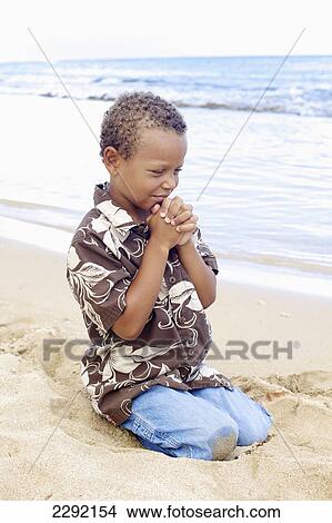 Picture - A young boy with hands folded in prayer by the ocean; Hawaii united states of america. Fotosearch